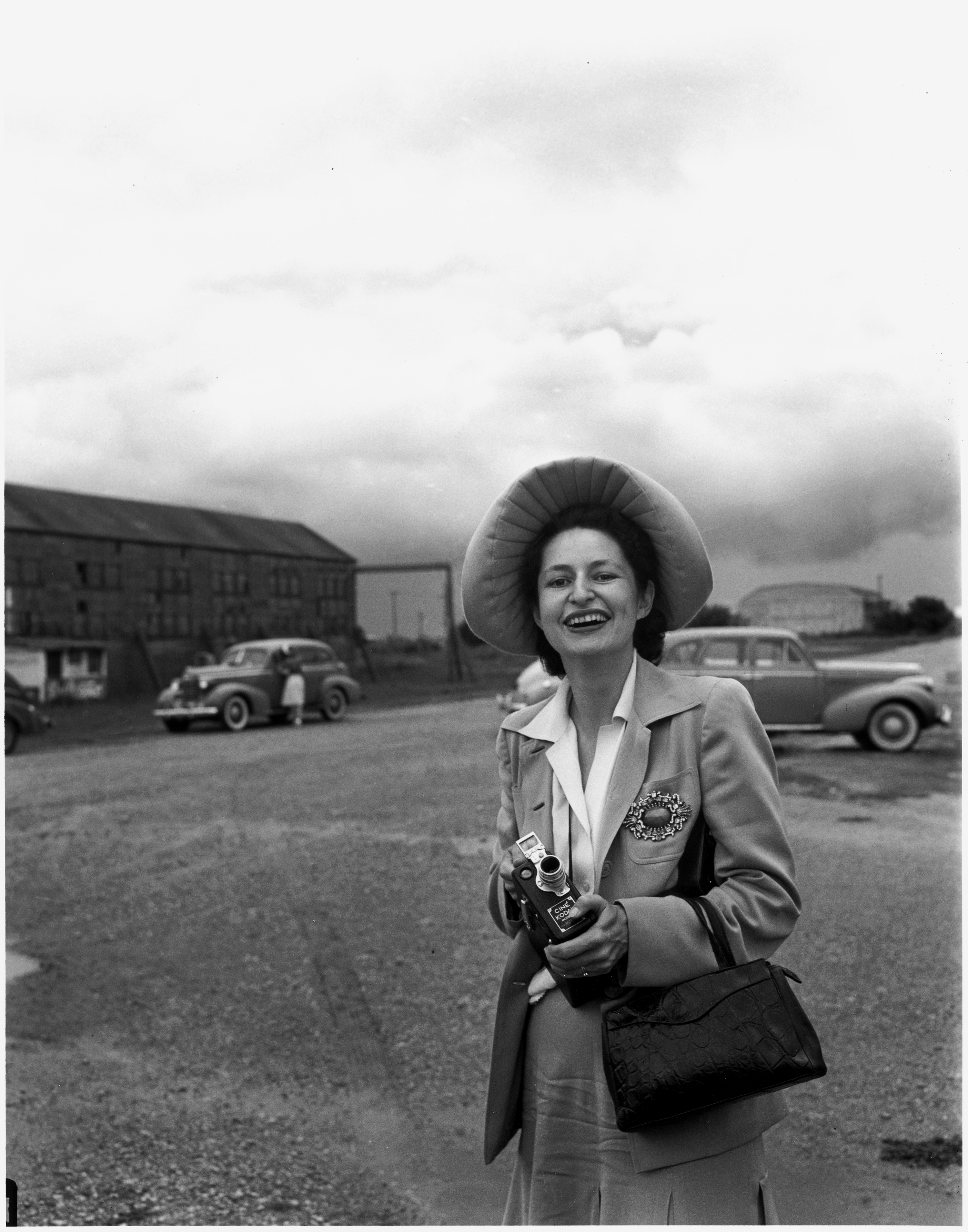 Lady Bird Johnson holding a movie camera and wearing a great hat in a parking lot
